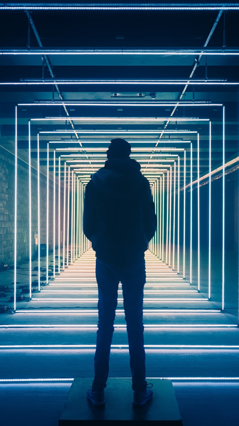 Silhouette standing at the center of a receding tunnel of glowing cyan and white rectangular neon light frames.