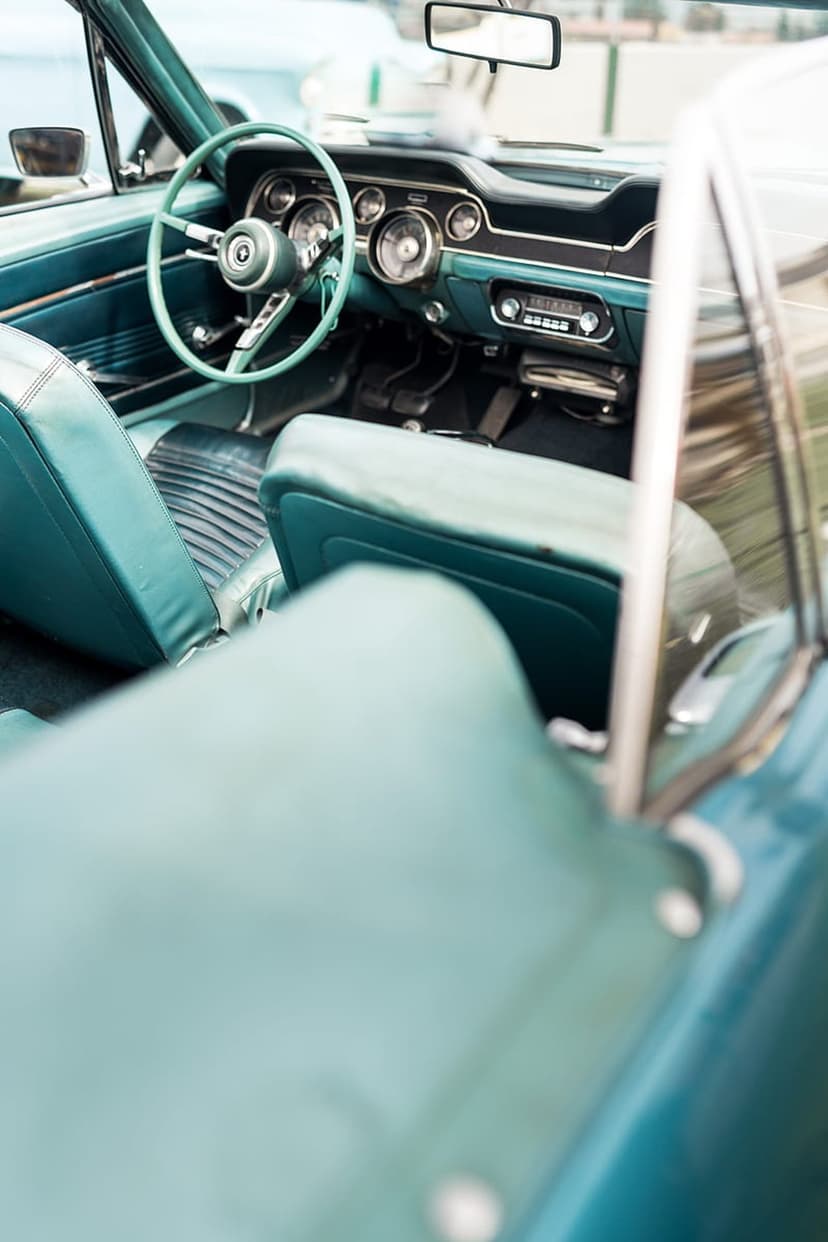Teal vintage car steering wheel and dashboard with soft upholstery under a clear blue sky through the glass.