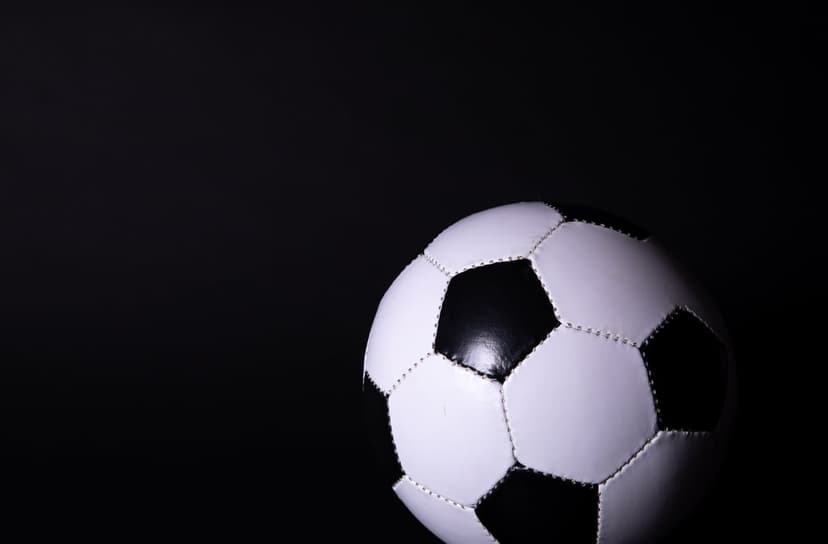 Monochrome soccer ball with detailed hexagonal panels and thick stitching resting against a solid black backdrop.