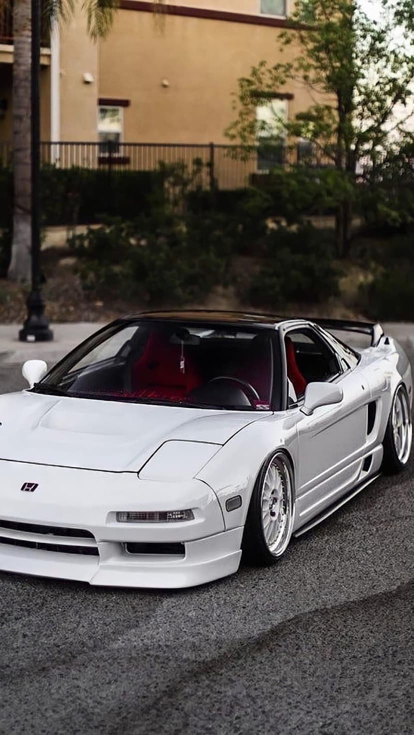 White Acura NSX with red seats and custom rims parked on asphalt, captured in a three-quarter front view.
