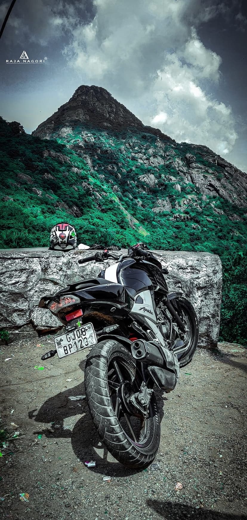 Black and white motorcycle parked on a gravel mountain road against a backdrop of green peaks and stormy clouds.