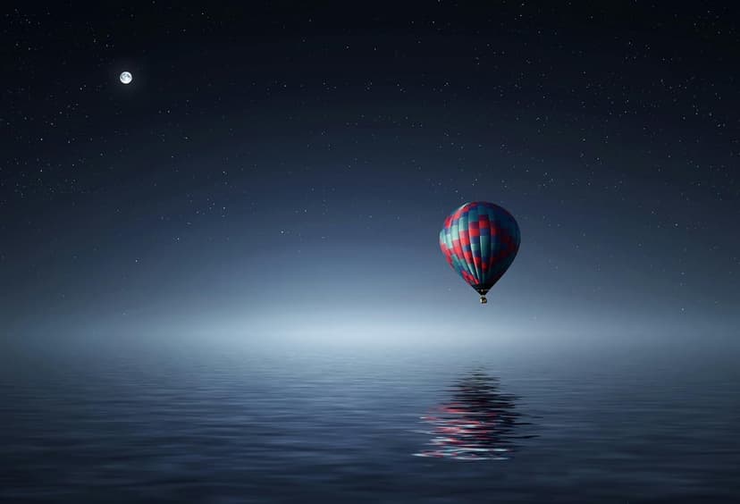 Hot air balloon drifting over calm water at night with a bright moon and stars reflecting on the glassy surface.