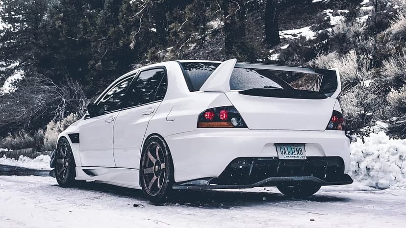 White Mitsubishi Lancer Evolution parked on a snowy mountain road with a backdrop of frosted pine trees in winter.