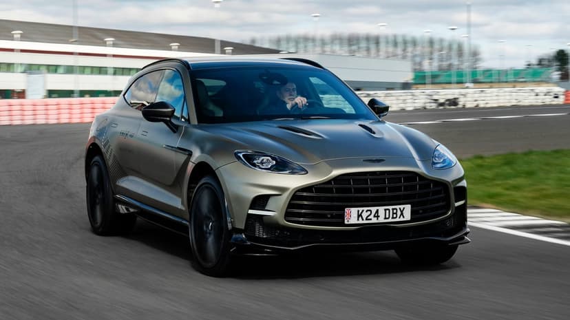 Matte grey Aston Martin DBX707 driving on a racetrack with motion blur and sharp front-end detail.