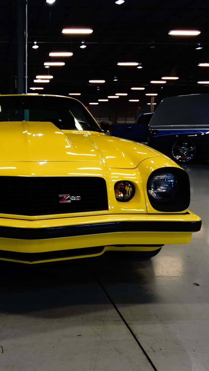 Yellow Z28 Camaro front fascia with a black grille and hood scoop parked inside a bright vehicle exhibition hall.