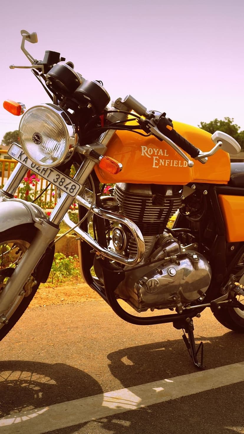 Orange Royal Enfield motorcycle with a chrome engine and brand logo parked on asphalt under a clear blue sky.