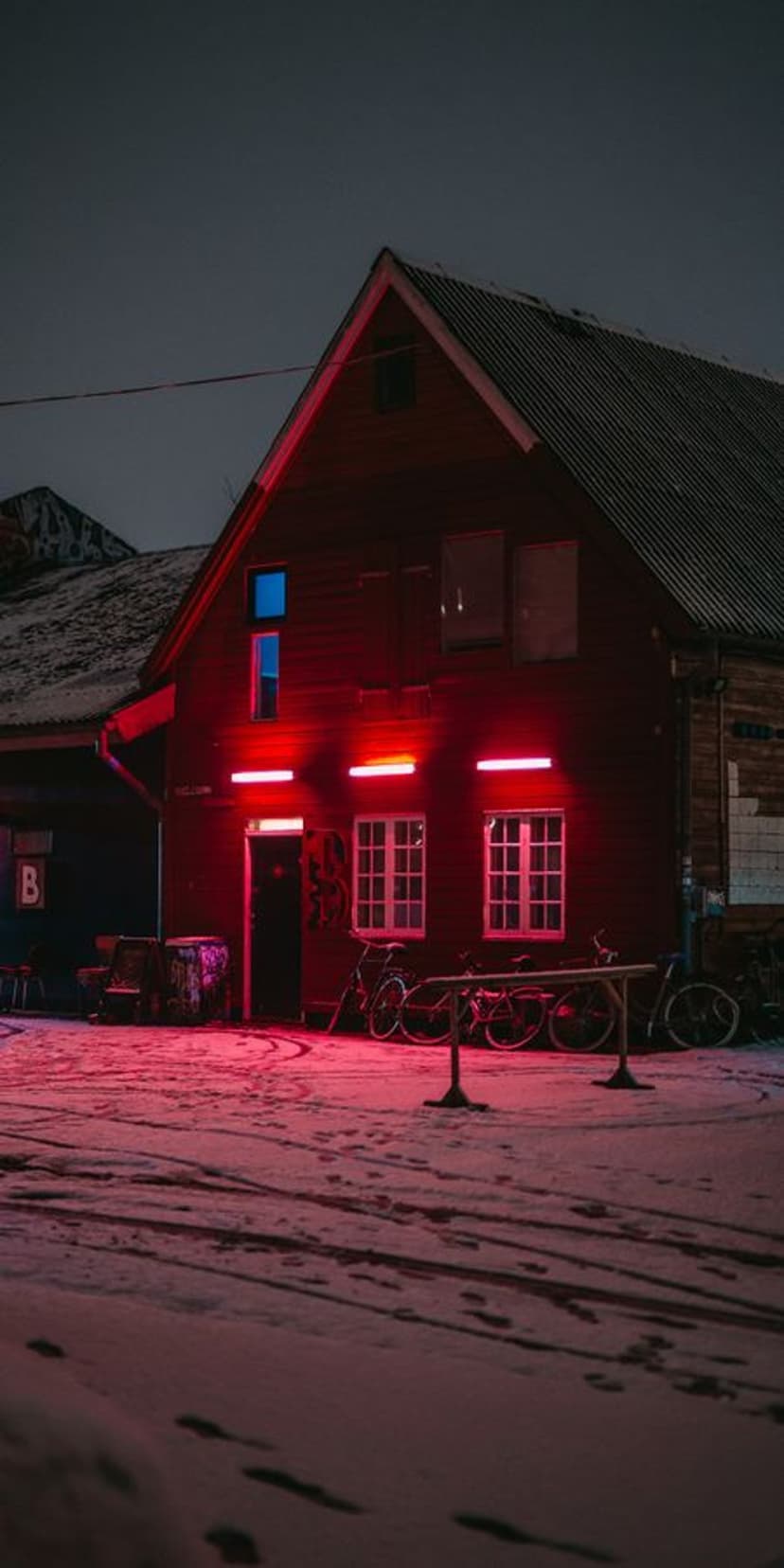 Red glowing building stands on a snowy street with parked bicycles under a dark winter sky at night.