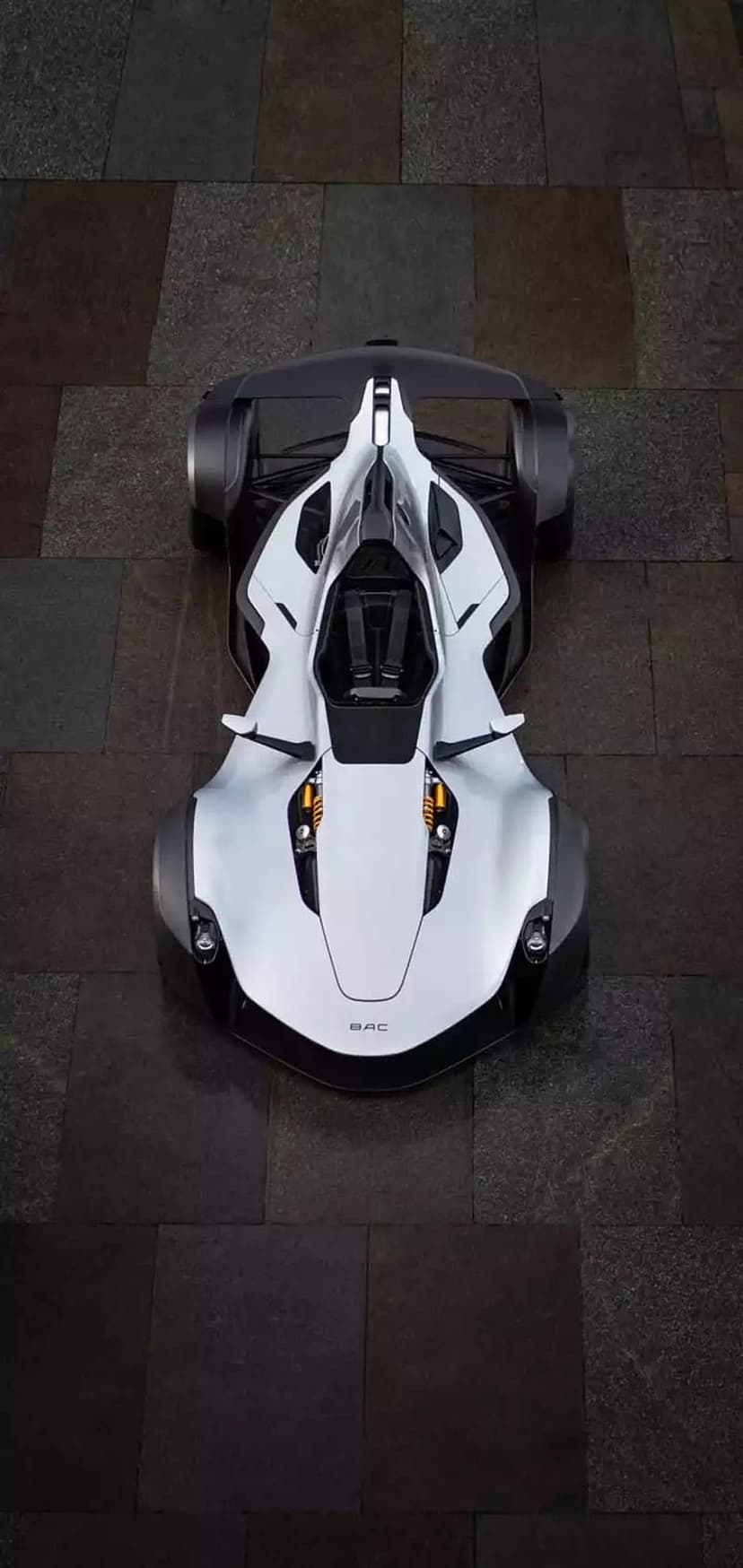 White BAC Mono single-seater sports car viewed from directly above on a dark, textured stone pavement.