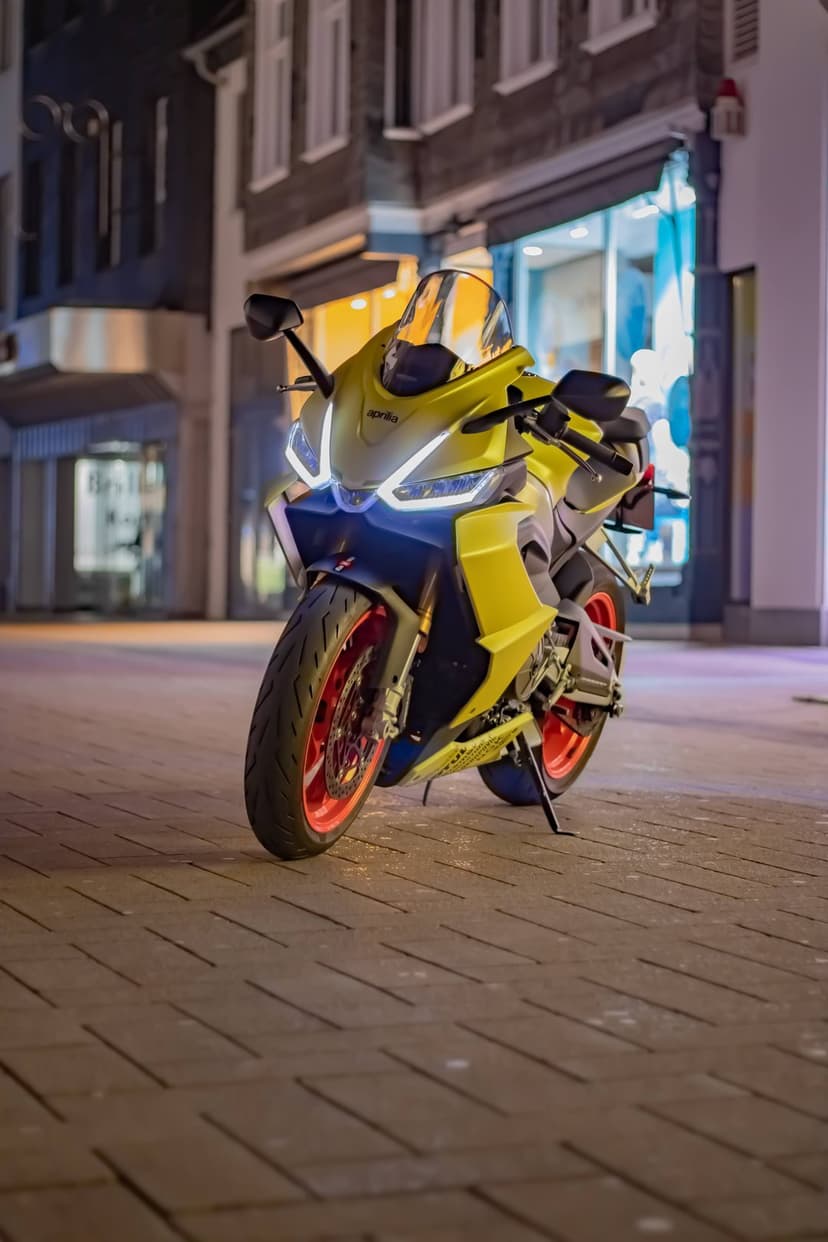 Yellow sport motorcycle with red wheels parked on a dark cobblestone street under glowing urban night lights.