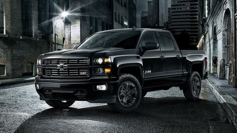 Black Chevrolet Silverado Z71 pickup truck with glowing headlights in a dark urban alley at night with city lights.