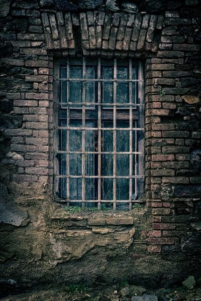 Grill-covered weathered window in old brick wall