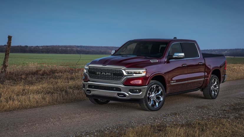 Burgundy Ram 1500 Limited truck parked on a dirt road between dry grass and green fields under a blue sky.