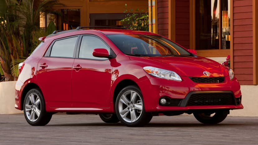 Red Toyota Matrix hatchback parked on a wooden boardwalk in front of a rustic red building with palm trees.