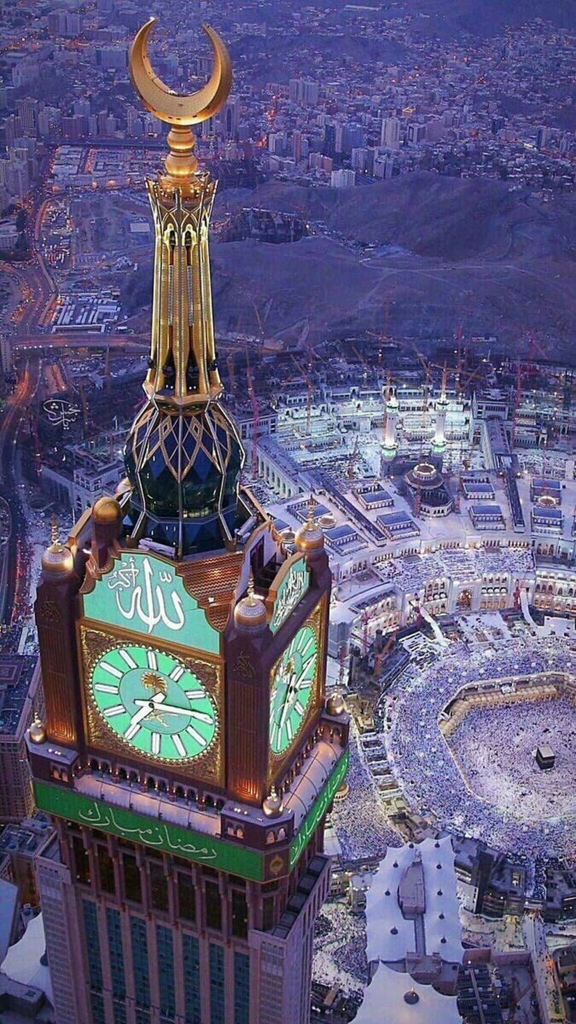 Makkah Clock Tower at dusk features a green Ramadan Mubarak banner above the crowded Masjid al-Haram courtyard.