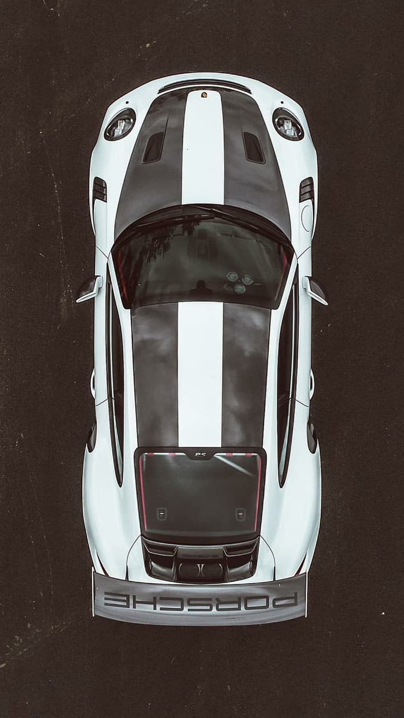 White Porsche 911 GT3 RS with black racing stripes seen from directly above, highlighting the large rear spoiler.