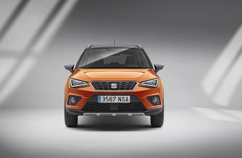 Frontal view of an orange Seat Arona SUV with black roof and LED lights in a minimalist grey studio.