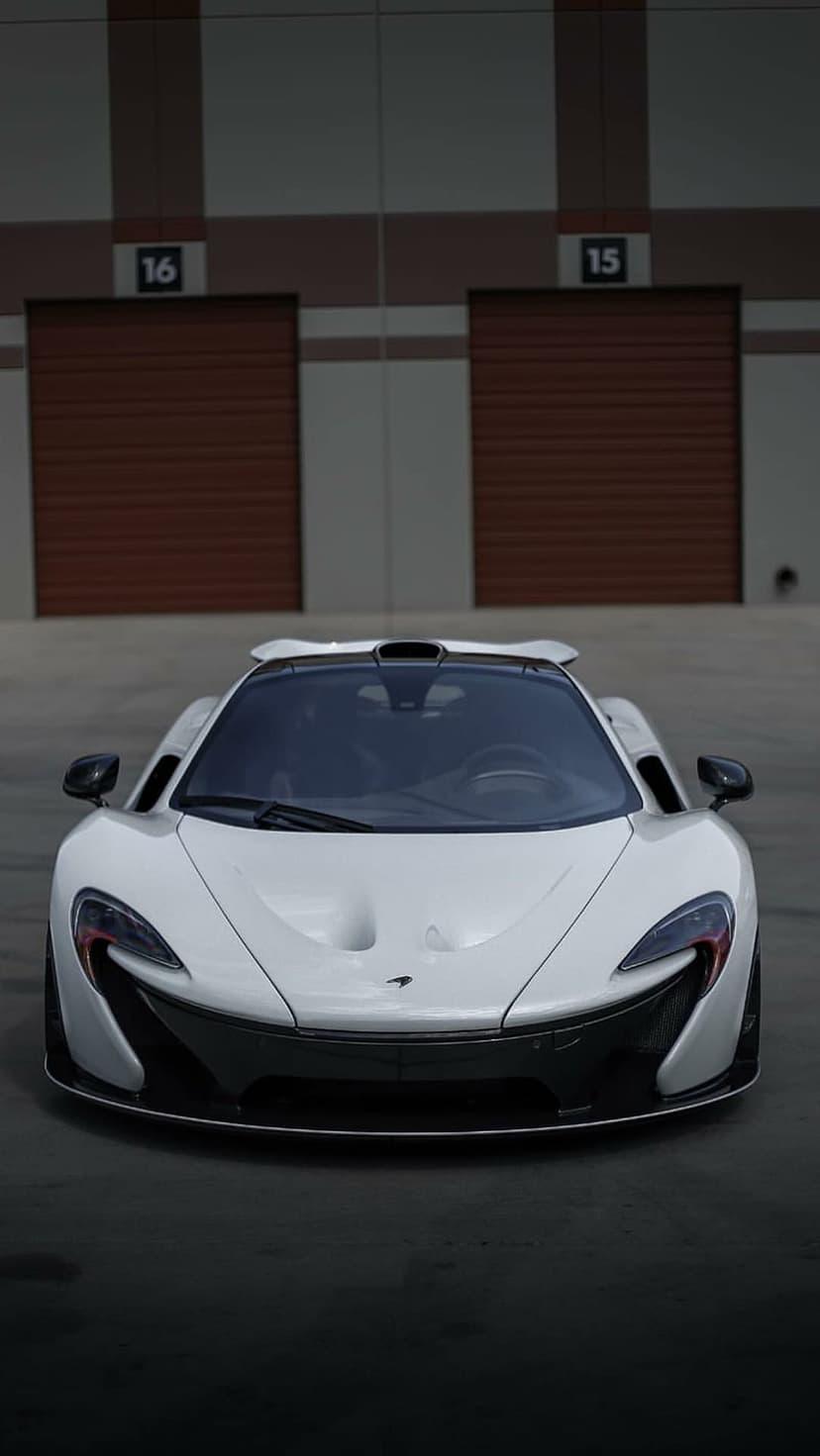 White McLaren P1 hypercar parked on concrete in front of brown ribbed storage unit doors under bright lighting.
