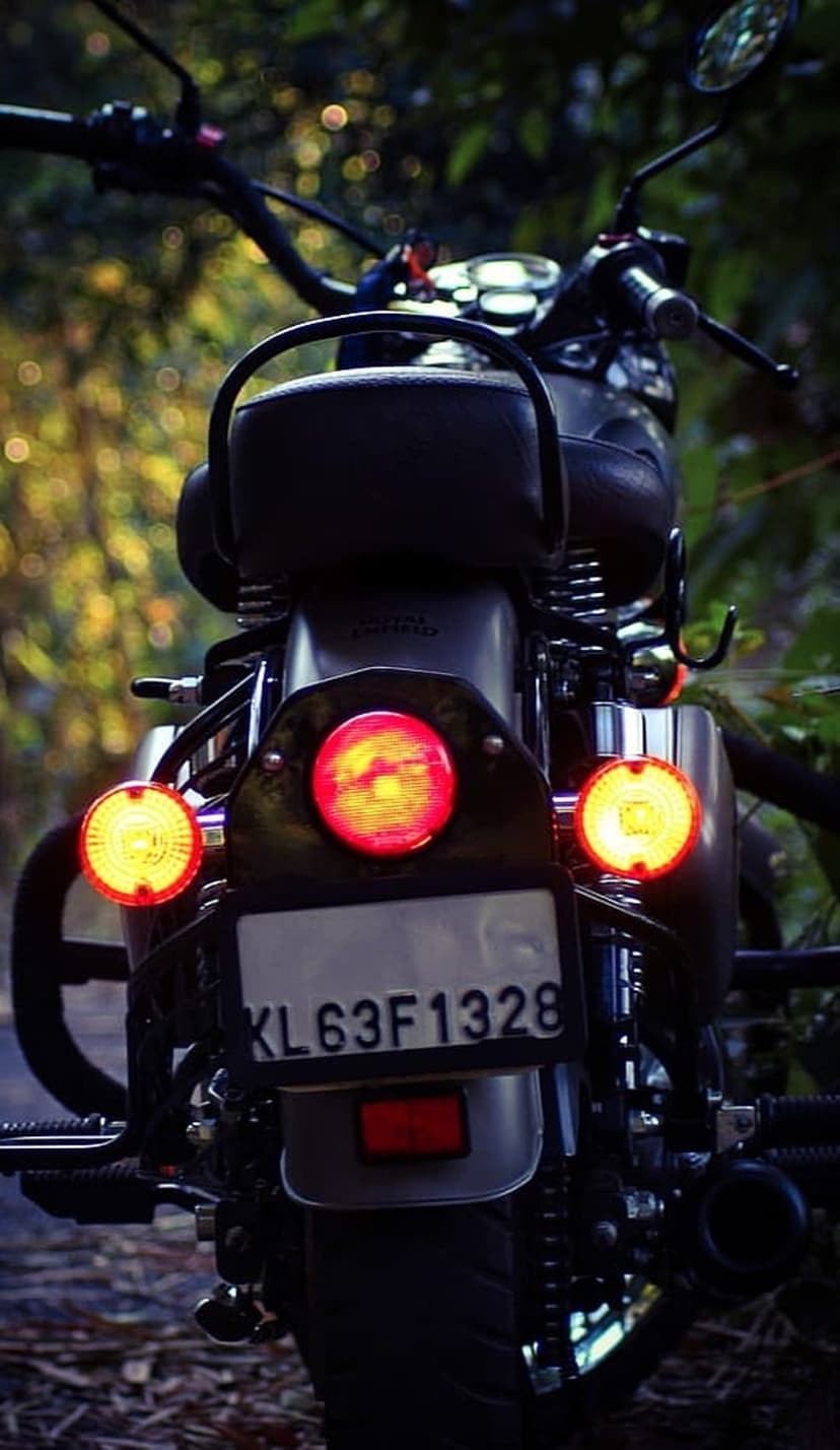 Royal Enfield motorcycle taillight and chrome fender in a close-up shot against a blurred green background.