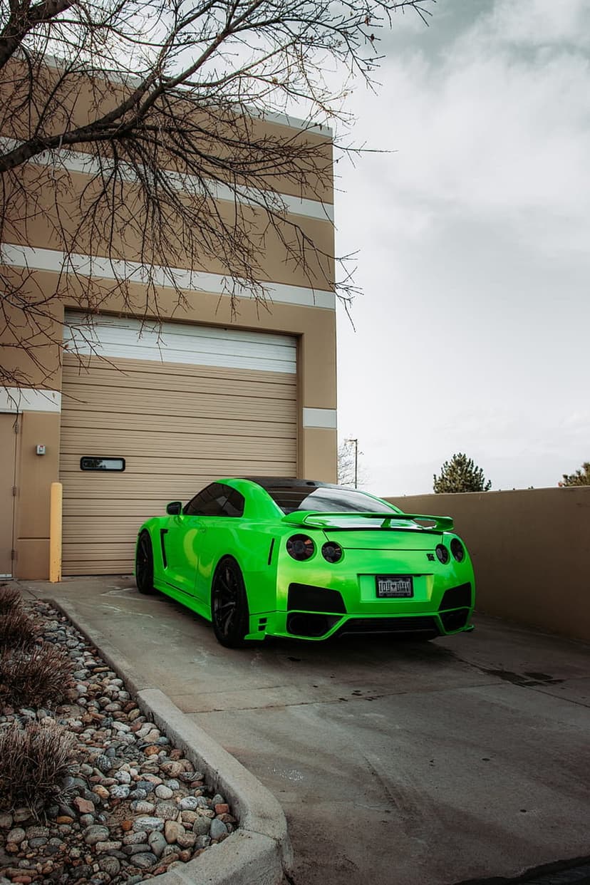 Lime green Nissan GT-R sports car parked in front of an industrial garage door with rocky landscape details.