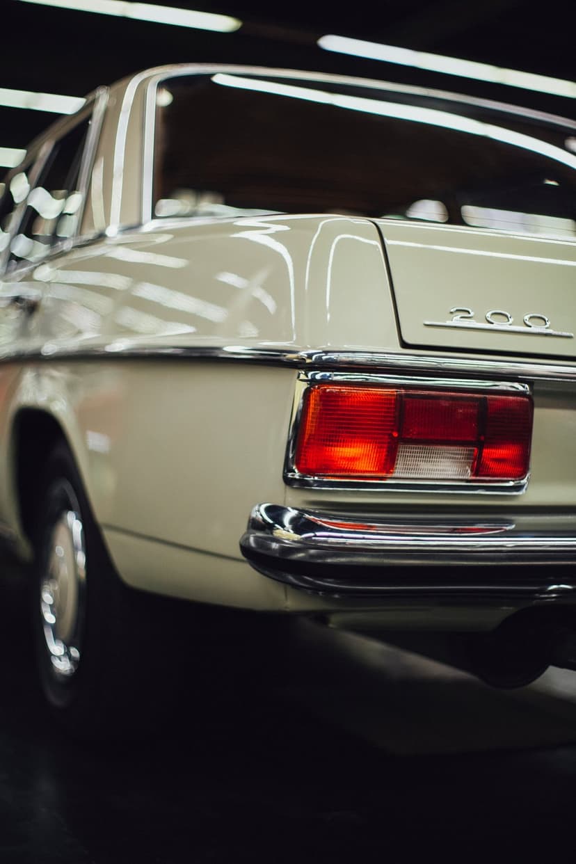 Mercedes-Benz 200 rear taillight and polished chrome bumper on a beige vintage sedan with metallic details.