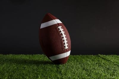 American Football on Green Grass Against Dark Background