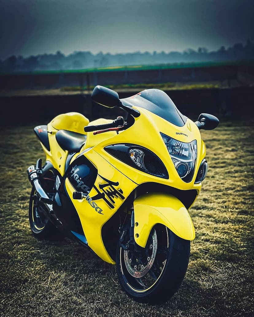 Suzuki Hayabusa motorcycle in bright yellow parked on a dry grassy field under a moody and misty overcast sky.