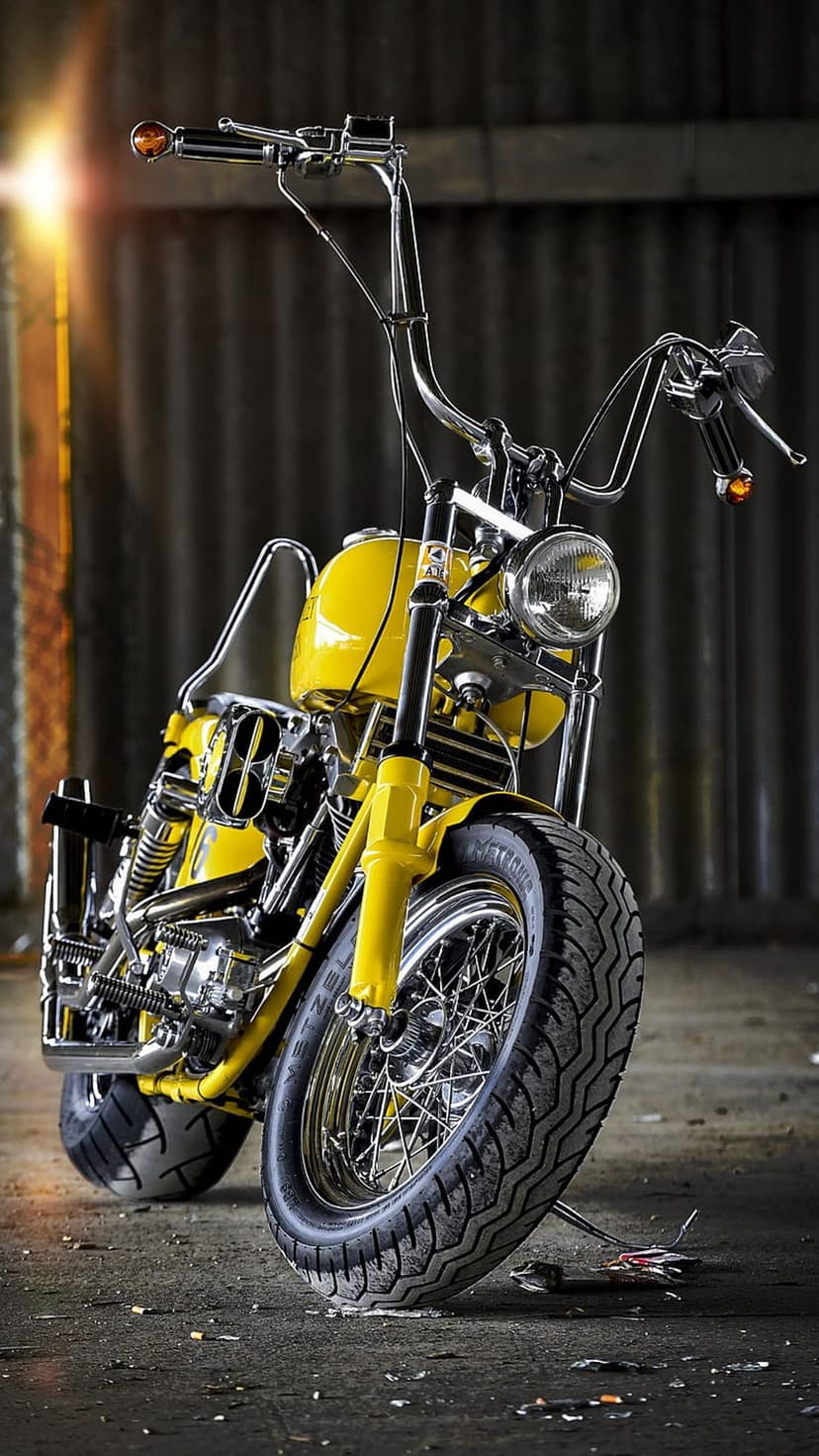 Yellow custom chopper motorcycle with high handlebars in a dimly lit industrial garage with chrome details.