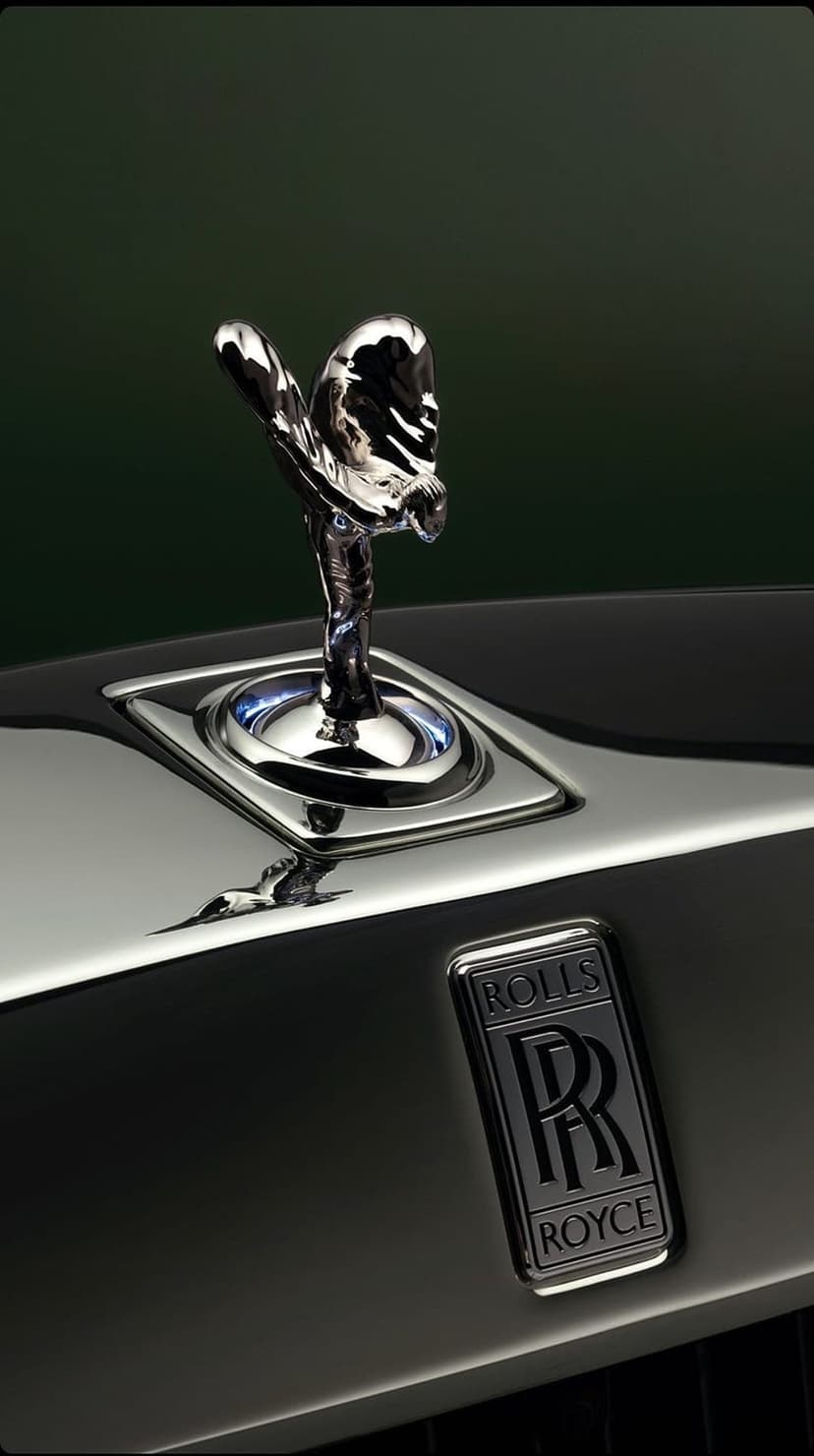 Spirit of Ecstasy sculpture and silver RR badge on a polished black car hood with sharp metallic reflections.