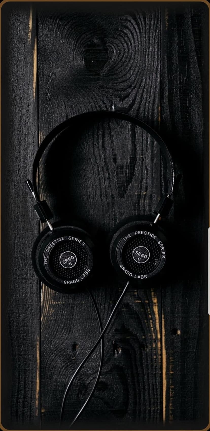 Grado SR60 S headphones featuring foam pads and metal mesh against a dark brown textured wooden background.