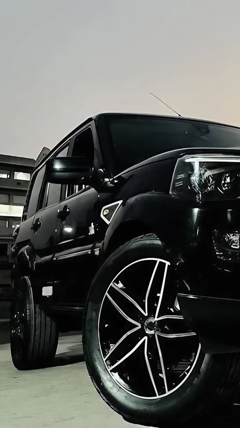 Black SUV with custom alloy wheels parked in an urban industrial zone during the hazy light of twilight.