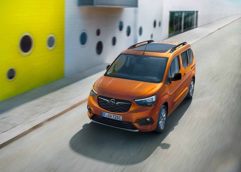 Orange Opel electric van driving on a road beside a modern white and yellow building with round windows.
