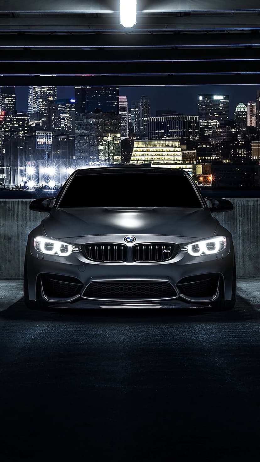 BMW M4 with glowing headlights parked on a dark city street with blurred skyscrapers and neon reflections.
