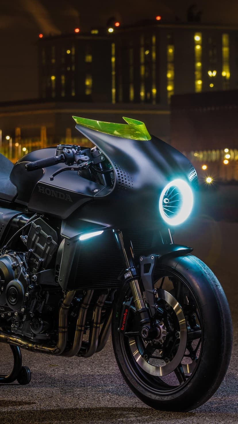 Matte black Honda motorcycle with a glowing blue LED headlight and lime green trim against city bokeh lights.