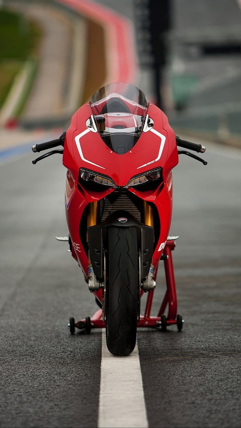 Red Ducati superbike with gold forks and LED headlights rests on a wet racetrack with red and white markings.