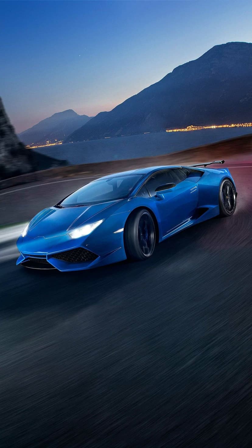 Blue Lamborghini Huracan driving on a mountain road at dusk with glowing headlights and blurred wheels.