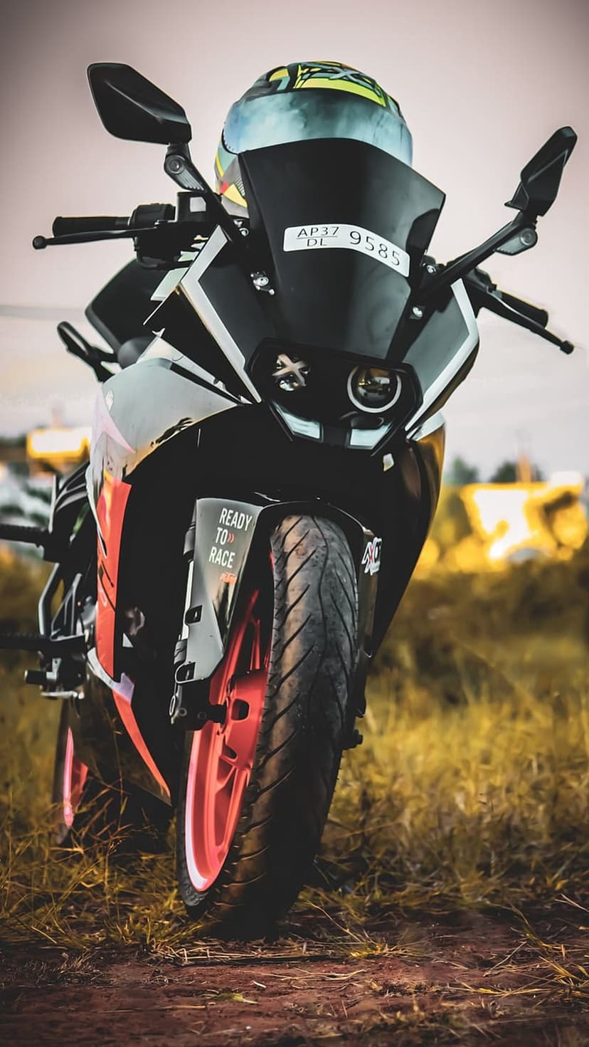 Black and orange KTM RC motorcycle with a colorful helmet on the handlebars, parked on a dirt path at sunset.