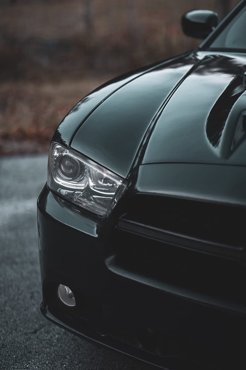 Black Dodge Charger headlight and sculpted hood with vents shown in a detailed close-up automotive shot.
