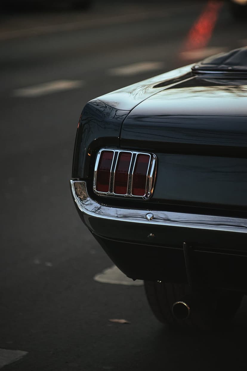 Vintage black Ford Mustang rear detail showcasing a red three-bar taillight and a reflective chrome bumper.