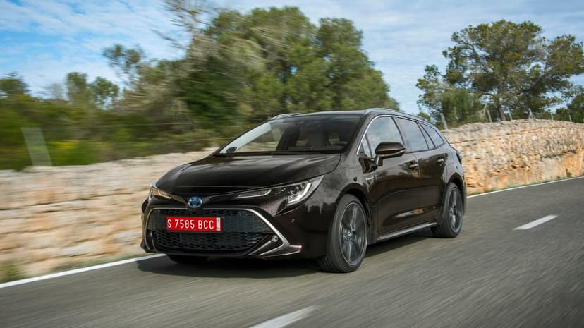 Dark brown Toyota Corolla Touring Sports hybrid driving on a coastal road with motion blur and stone wall background.