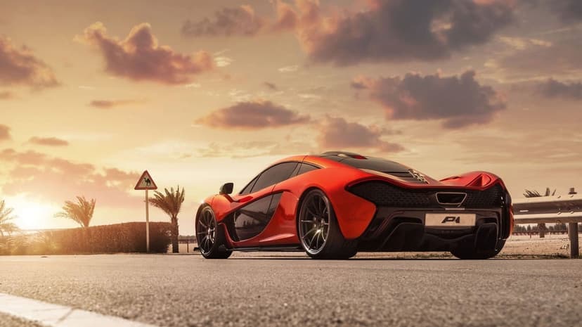 Red McLaren P1 supercar parked on a desert road under a golden sunset sky with palm trees and soft clouds.