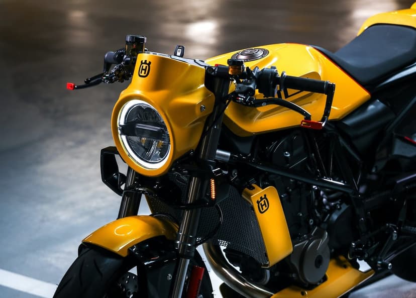 Close-up of a yellow Husqvarna motorcycle with a circular LED headlight and black handlebars in a dark garage.