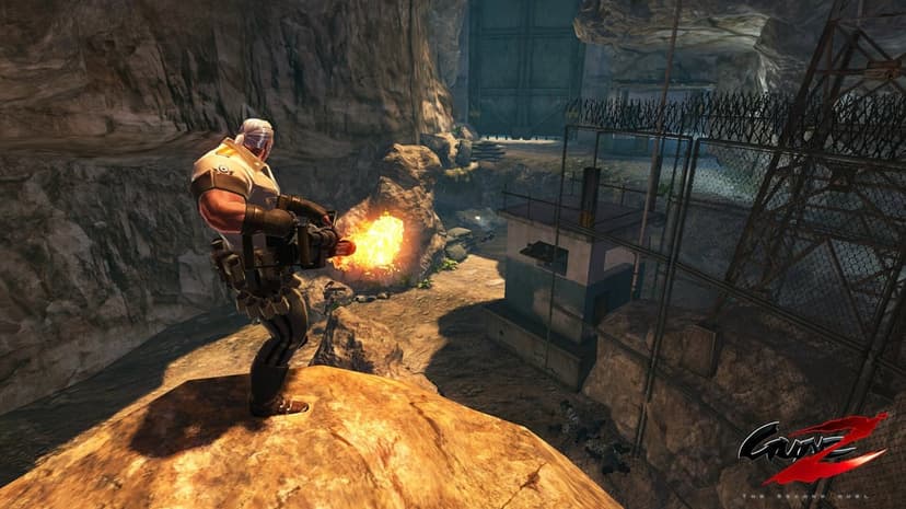 Muscular soldier firing a flaming heavy weapon from a rocky cliff overlooking a detailed military base in GunZ 2.