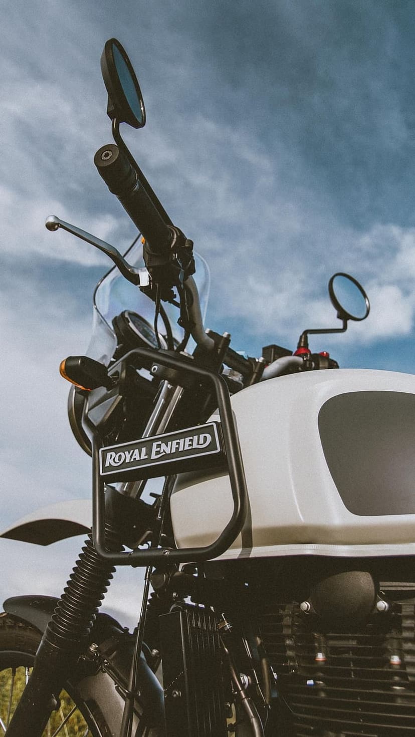 White Royal Enfield handlebars, windscreen, and rack seen from a low angle against a cloudy blue sky.