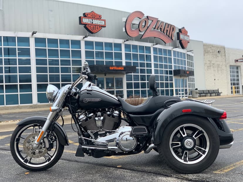 Black Harley-Davidson Freewheeler trike with chrome engine parked in front of a glass dealership building.
