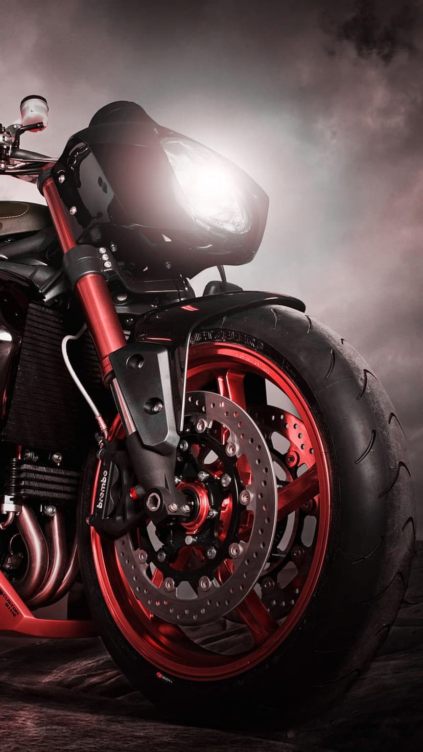 Red-spoked sportbike front wheel featuring Brembo disc brakes and a glowing headlight against a cloudy sky.