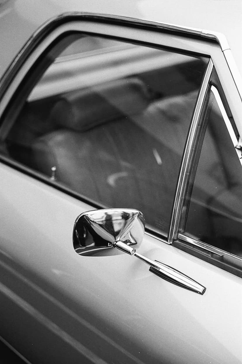 Chrome side mirror and window trim of a vintage car in a high-contrast black and white close-up shot.