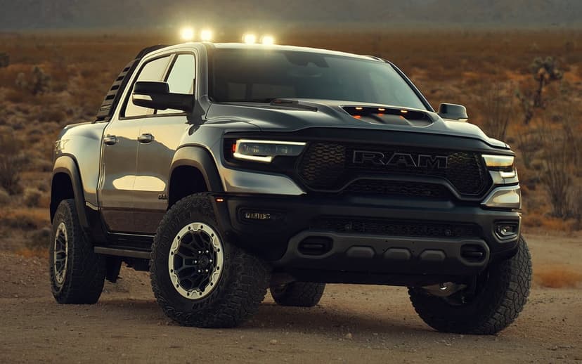 A gray Ram 1500 TRX off-road pickup truck with glowing roof lights parked on a dusty desert trail at sunset.