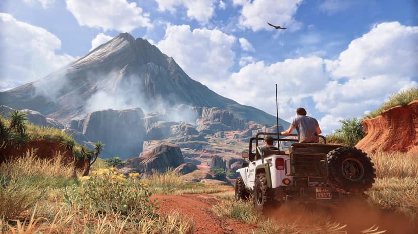 Men in a white jeep drive on a red dirt path toward a giant smoking volcano under a cloudy blue sky.