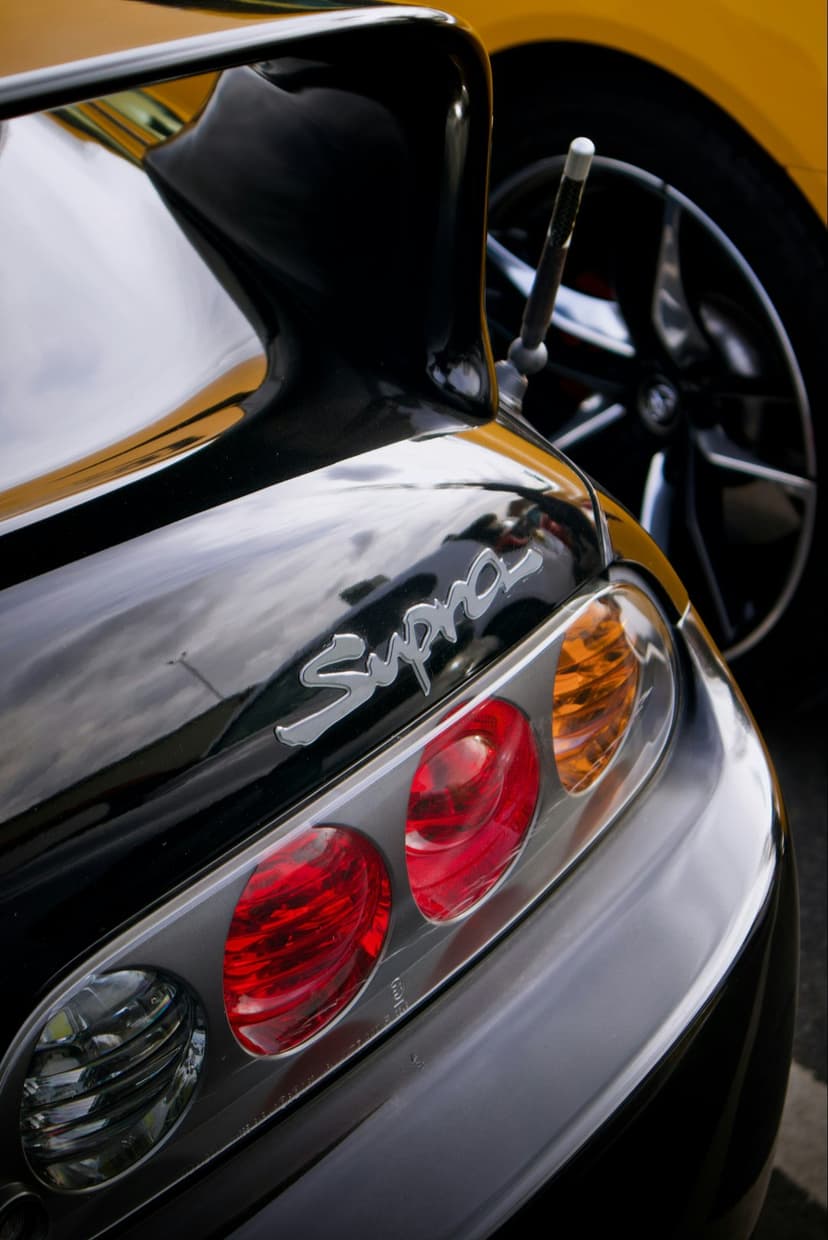 Toyota Supra circular taillights and chrome rear badge shine on black bodywork with a bokeh street background.