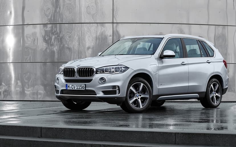 Silver BMW X5 SUV parked on a wet surface in front of a reflective metallic wall under soft lighting.